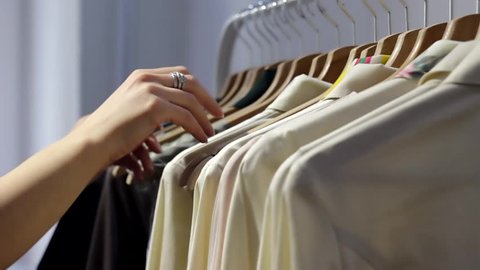 Woman's hands run across a rack of clothes, browsing in a boutique.