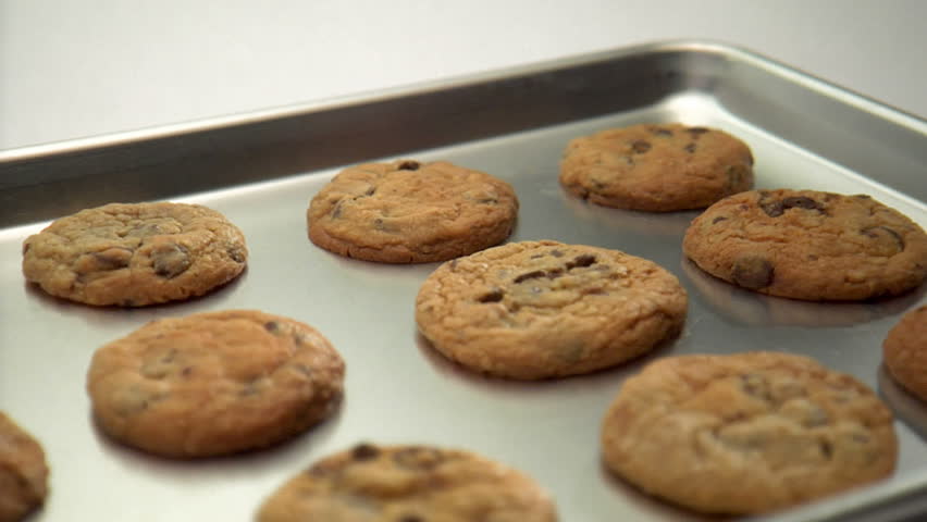 pan over tray of chocolate chip cookies, hand reaches in to pick up one cookie