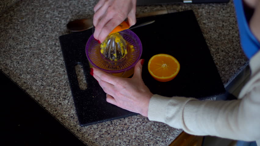 Woman making orange juice in the kitchen, close-up. Top view