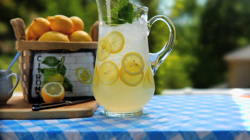 Man placing 2 glasses of lemonade by Pitcher of lemonade on table outside