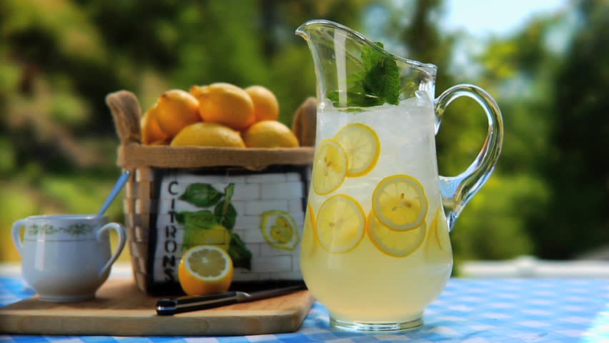 Man placing 2 glasses of lemonade by Pitcher of lemonade on table outside