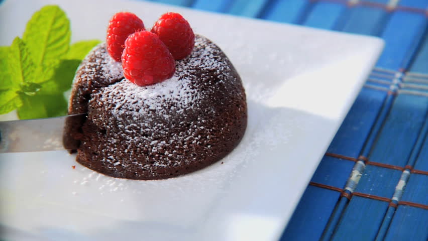 Cutting into chocolate lava cake with raspberries and mint