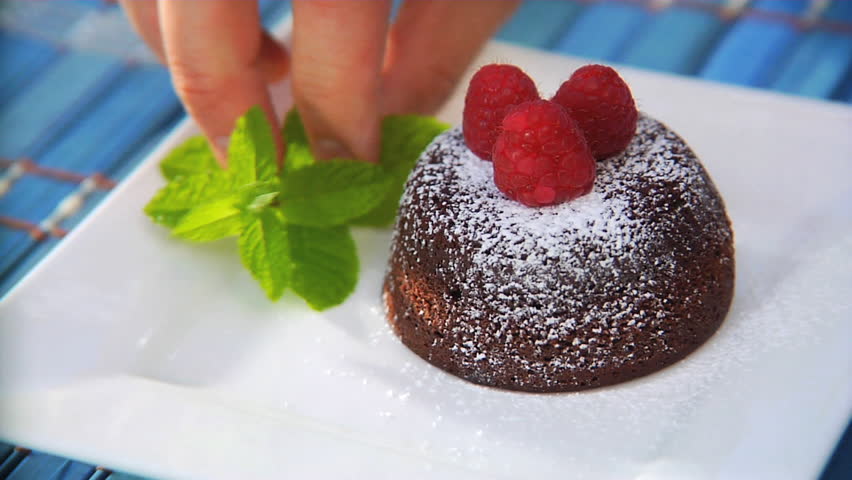 Sprinkling powdered sugar over chocolate lava cake with raspberries and mint