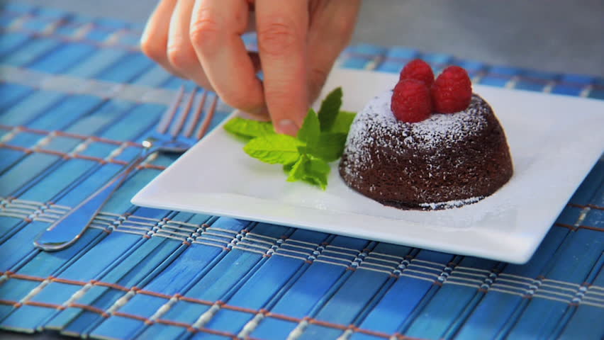 Sprinkling powdered sugar over chocolate lava cake with raspberries and mint