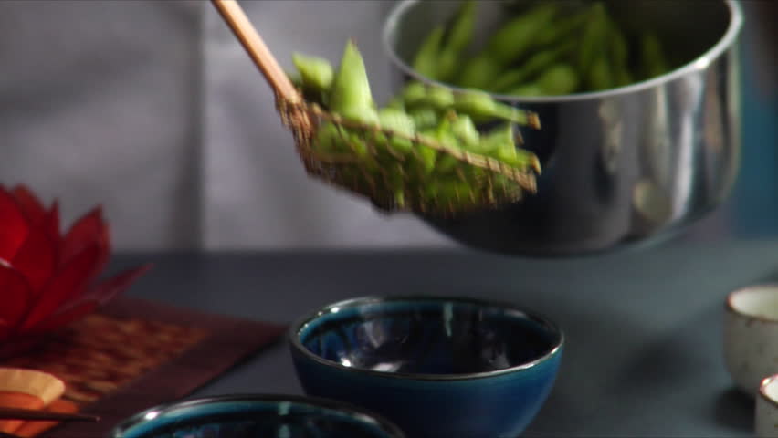 Pan from left to right of chef dishing up steaming hot Edamame (soy beans).