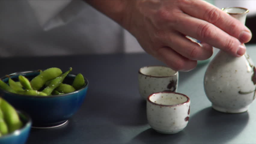 Close-up of chef pouring hot sake with bowls of Edamame (soy beans) on the side.