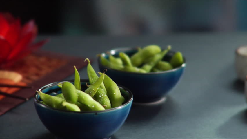 Slow pan over Asian place setting, bowls of Edamame (soy beans) and sake set.