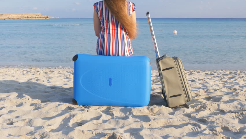 Young woman with a suitcase sitting on the beach