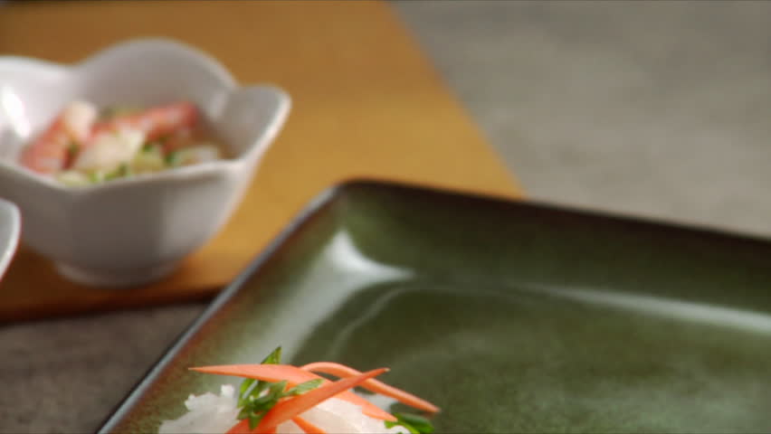 Close-up pan over cucumber salad as chef places four shrimp tempera onto serving