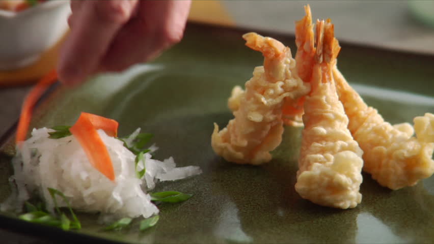 Pan over chef garnishing shrimp and cucumber salad landing on plate of shrimp
