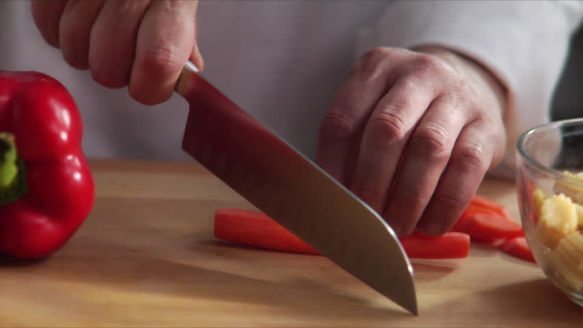 Close-up of chef chopping a carrot with red pepper on cutting board.