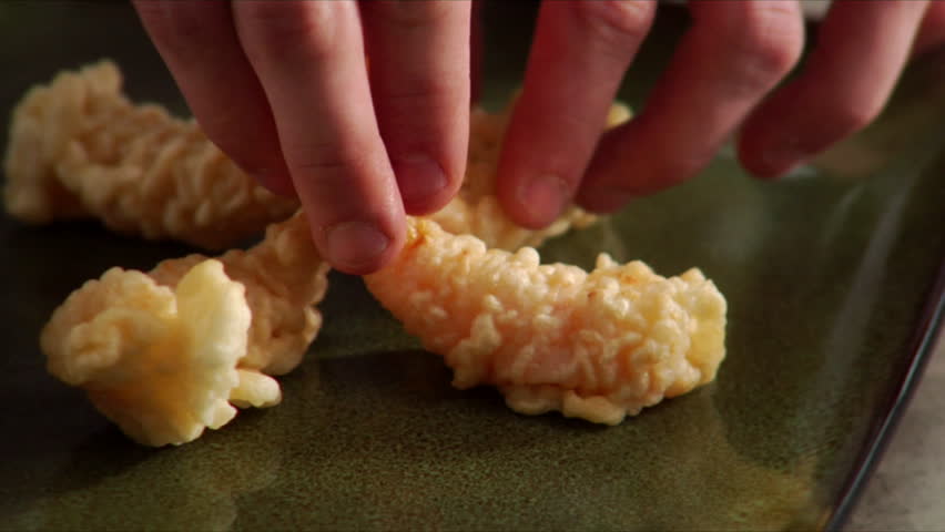 Extreme close-up of chef placing tempera shrimp on serving platter.