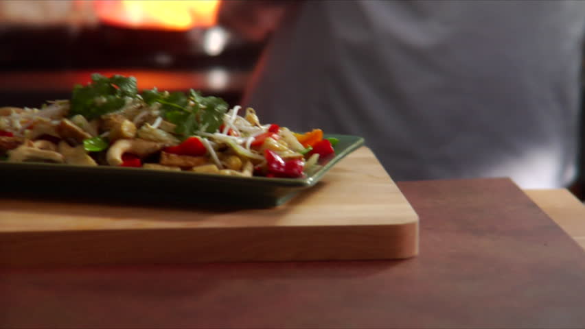 Slow pan over a plate of Asian stir fried vegetables with chef flaming wok in