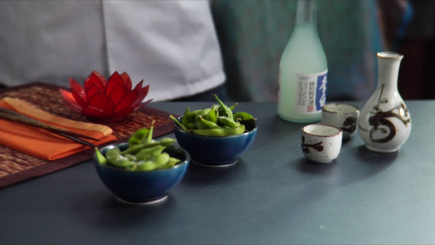 Lock down shot of chef pouring hot sake with bowls of Edamame (soy beans) on the
