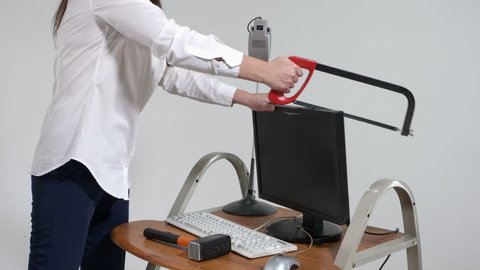 Crazy office worker destroying desktop computer with hacksaw and sledgehammer