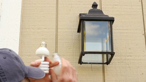 Man outside changing an incandescent light bulb to a CFL light bulb in an outdoor light fixture to save energy.