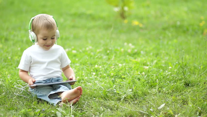Happy child with a tablet PC sitting on the grass
