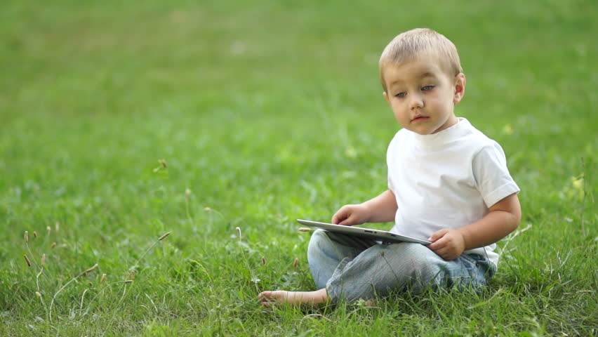 Baby boy working with the Tablet PC sitting on the grass

