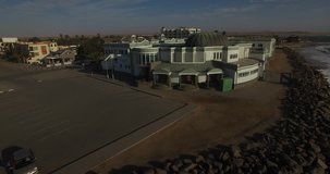 Drone video of view of Namibian Atlantic coastline, Swakopmund town buildings, beach, old pier, surf break point and landscape of ocean background of Swakopmund holiday resort at Namibia's west coast