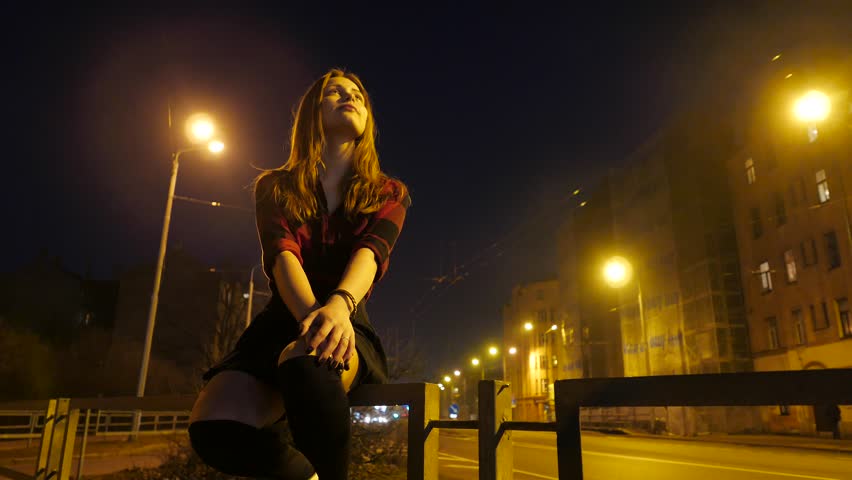 Modern cute teen girl sitting at night in a city and enjoy warm days of ear...