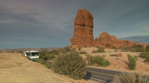 RV driving past Balanced Rock formation at Arches 