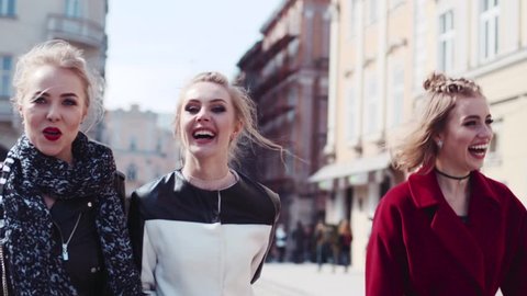 Happy three friends wandering in the old city center, laughing, and joking. The woman in a red coat hugs her friend. Stylish modern women. Having fun with true friends.