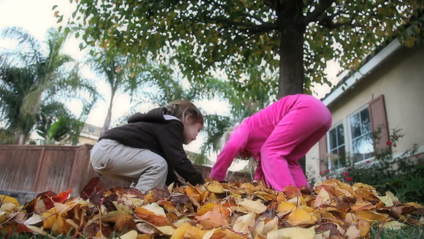 Two little girls throwing fall leaves in the air
