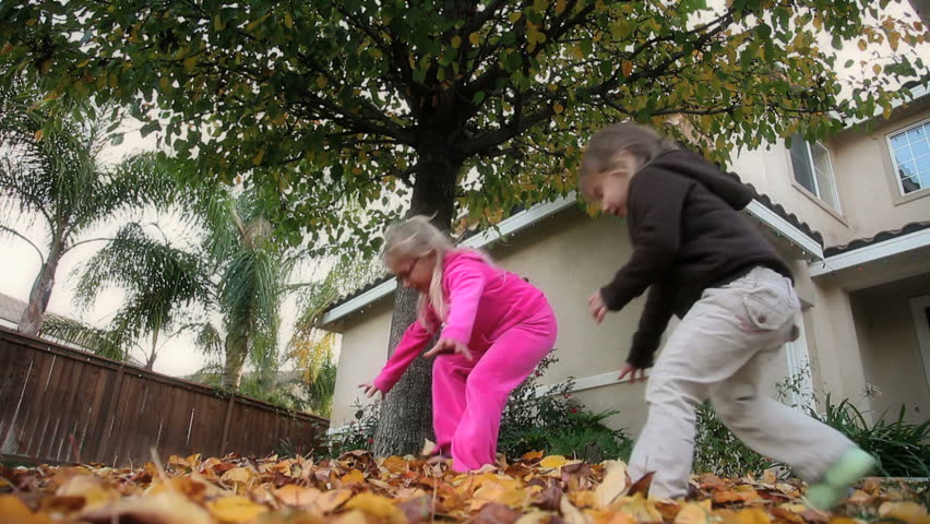 Two little girls throwing fall leaves in the air