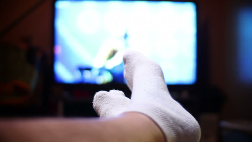 A man watches television, relaxing with his feet up.  Extreme shallow DOF.