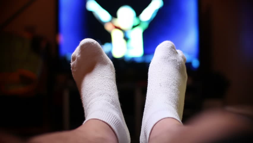 A man watches television, relaxing with his feet up.  Extreme shallow DOF.