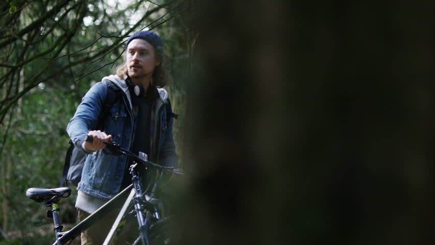 4K Young man walking his bike through a forest