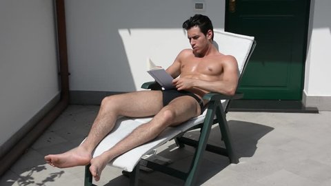 Shirtless Young Man Drying Off in Hot Sun Reading a Book, Muscular Man Wearing Bathing Suit Sunbathing on Beach Lounge Chair