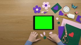 Overhead lockdown footage of woman arranging artificial flower with fabric on wooden table. Aerial video of female making craft by digital tablet with green screen. Flat lay of art product by female.
