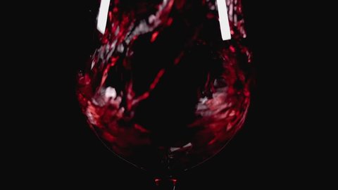 Filling wine glass with red wine super slow motion macro shot, black background