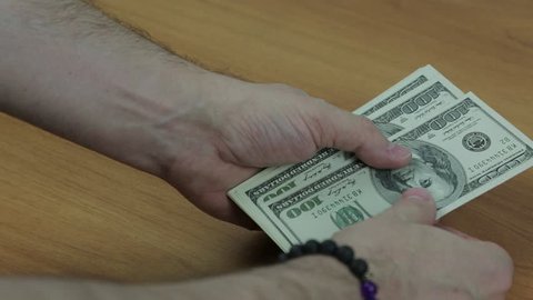 Men's hands with a bracelet count the hundred-dollar bills