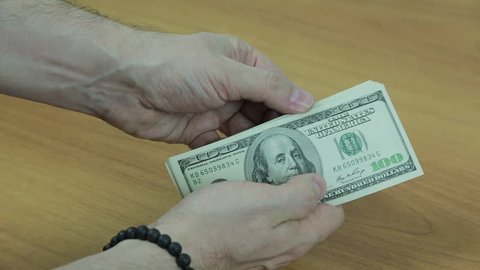 Men's hands with a bracelet count the hundred-dollar bills