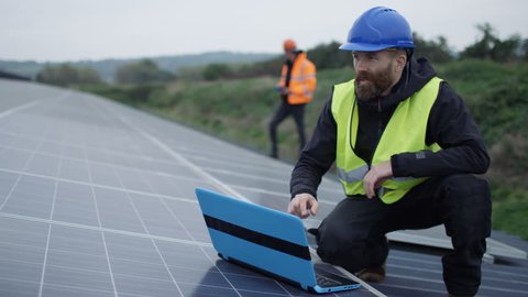 4K Technician with laptop checking the panels at solar energy installation