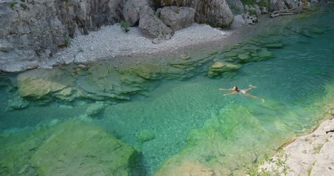 Top view Young woman swimming in river gorge Athletic swimmer girl relaxing in crystal clear blue water on bright sunny summer day enjoying nature outdoors