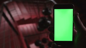 Close-up of a man holding the phone with a vertical green screen in the background red stairs