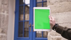 Closeup hand of man holding tablet computer with vertical green screen in the background blue door