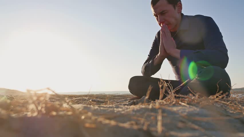 religion. Man praying sitting on the ground at sunset sun silhouette religion