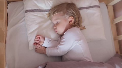 Peaceful adorable baby sleeping on his bed in a room at home. Soft focus. Sleeping baby concept. 2 year-old babyboy sleeps at home, top view