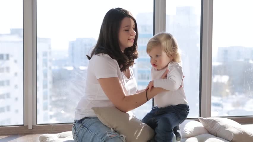 Mother and her baby son having fun and playing at home. Little kid 2 years old play with his mom arms at home near a big window