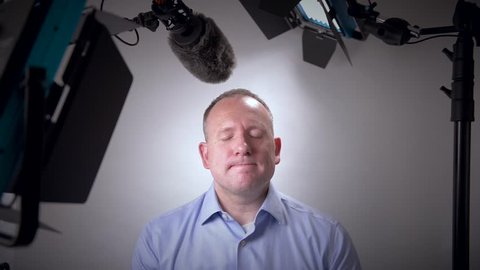 Nervous and awkward business man about to be interviewed on camera in a studio forgets his lines.