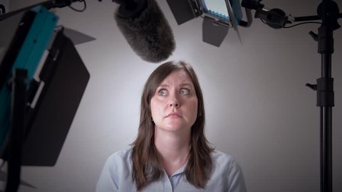 Scared business woman about to be interviewed on camera in a studio with video lights and microphone.