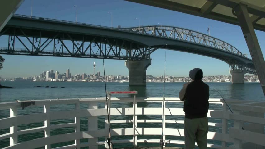 Angler fishing at Northcote point wharf in front of the Auckland Harbour bridge