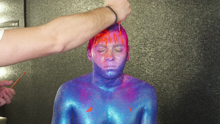 Body art maker pouring orange paint to man's face and hair