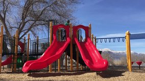 A playful video of two children sliding down slide at a park. The warm spring weather invites children to the playground.