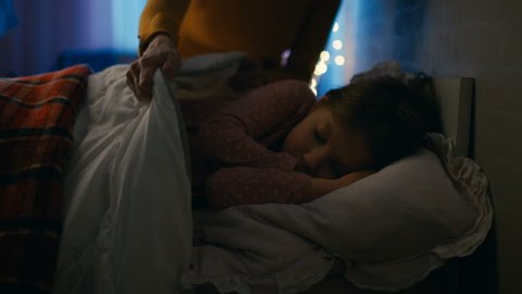 Sweet Little Girl Sleeps in Her Bed at Night, Her Mother Tucks Her Blanket in. Shot on RED EPIC-W 8K Helium Cinema Camera.