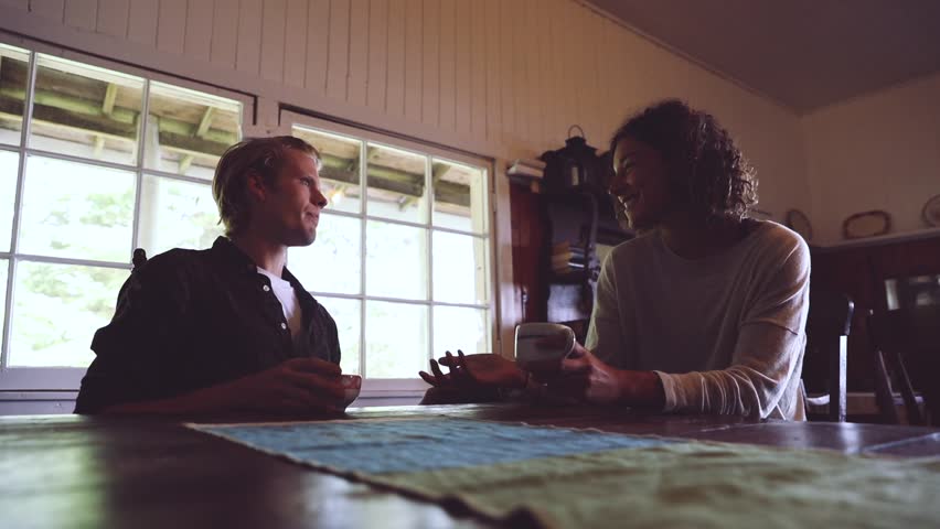 Young couple drinking coffee in a old wooden cabin in Canada. Blond man looking at his girlfriend and smiling, both holding a cup of coffee or tea. Love and relax concepts.